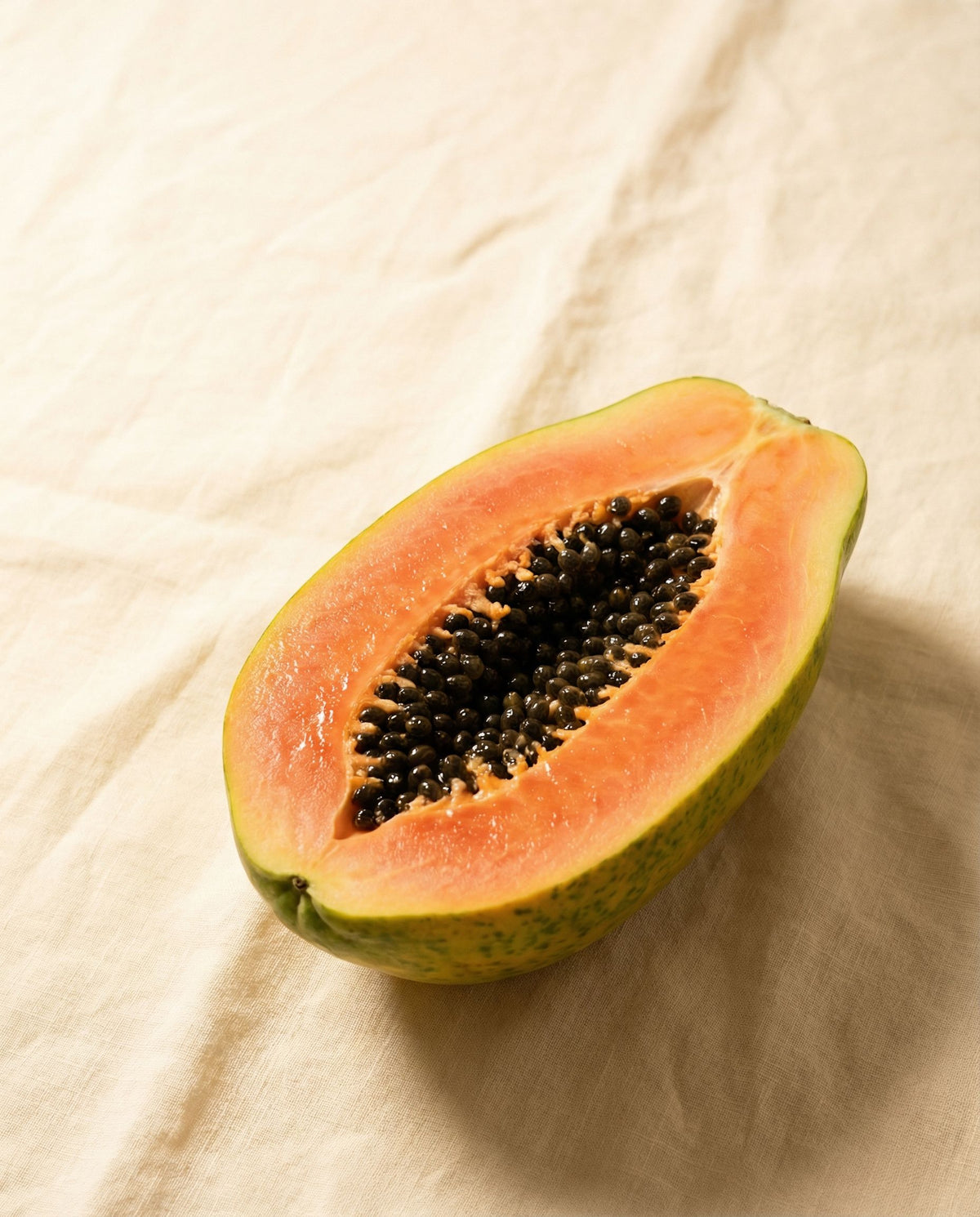 Halved fresh papaya on a warm cream linen surface in morning light