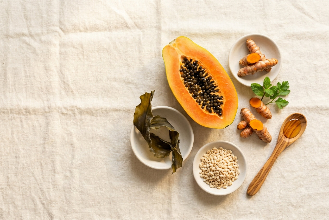 Overhead arrangement of whole plant ingredients - fresh roots, leaves, seeds, and fruit - laid out on a warm linen surface in natural light.